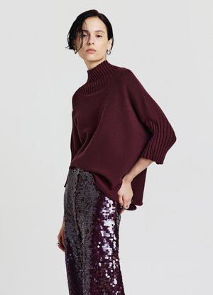 Maglione a maglia bordeaux con colletto alto a coste e vestibilità ampia, abbinato a una gonna lunga fino al pavimento in tonalità di viola scuro e argento, decorata con paillettes.