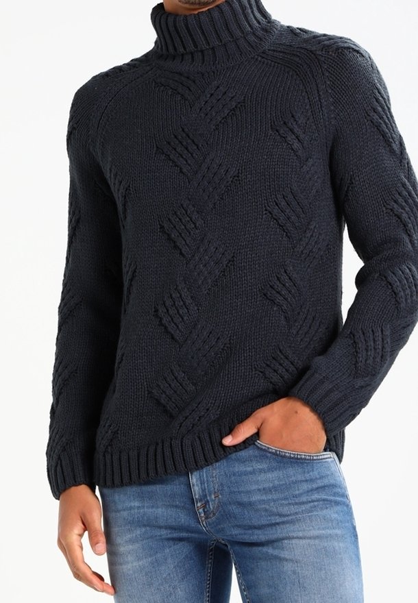 Fetter gestrickter navyfarbener Rollkragenpullover mit strukturiertem Rautenmuster, gerippten Bündchen und Saum. Kombiniert mit hellblauen Jeans.