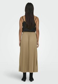 Top negro sin mangas y falda máxima plisada beige. La falda tiene una cintura alta y cae a mitad de la pantorrilla, acompañada de botas negras hasta el tobillo.