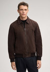 Bruine suede bomberjack met een rits aan de voorkant, puntige kraag, ribgebreide manchetten en een ribgebreide taille. Het jasje heeft zijzakken en een gladde textuur.