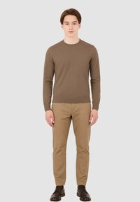Maglione marrone a maglia con scollatura rotonda, abbinato a pantaloni khaki e stivali marroni. Design semplice, forma attillata e polsini a coste.