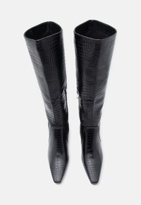 Bottes noires montantes en cuir synthétique avec un motif crocodile texturé, pointe pointue et fermeture éclair sur le côté. Doublure intérieure lisse.