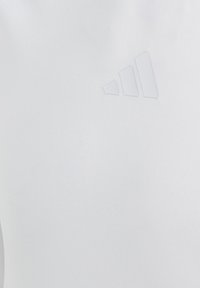 Witte sportshirt gemaakt van gladde, rekbare stof. Heeft een subtiele, tone-on-tone adidas-logo in de rechterbovenhoek.