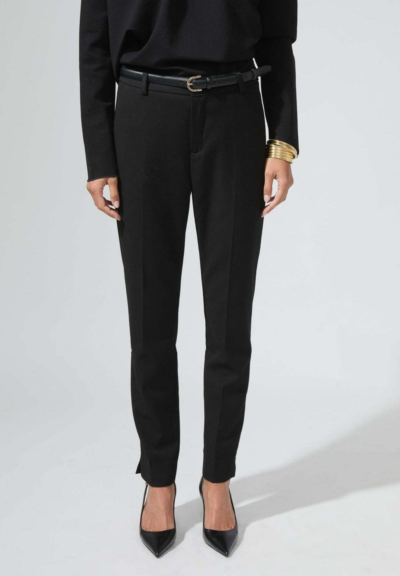 Pantalons noirs ajustés avec une coupe slim, présentant une coupe droite, des fentes sur les côtés aux chevilles, et une ceinture noire avec une boucle décorative.