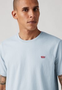 Lichtblauwe katoenen T-shirt met ronde halslijn en korte mouwen, met een klein rood Levi's-logo op de bovenste linkerkant van de borst.