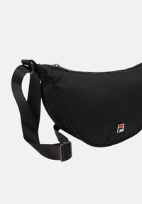 Svart nylon axelväska med en böjd design, zipförslutning och en logotyppatch. Justerbar rem med en metallklämma för att fästa.