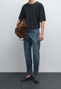 Svart kortärmad t-shirt, blå avslappnade jeans, svarta loafers, bärande en brun mockaväska. Enkel design, avslappnad stil, minimala detaljer.