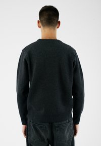 Ciemnoszary dziany sweter z długimi rękawami, ściągaczami na mankietach i na dole. Posiada okrągły dekolt i średnią teksturę. Widok od tyłu.