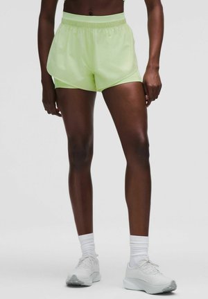Helle grüne Sportshorts mit lockerer Passform, elastischem Taillenbund und glatter Oberfläche. Kombiniert mit weißen Sneakers und Socken.