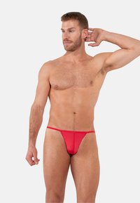 Punainen stringitanga, joka on valmistettu sileästä, joustavasta kankaasta. Minimalistinen malli, jossa ohuet hihnat ja vähäinen peittävyys. Yksinkertainen muotoilu ilman lisäkuvioita tai koristeita.