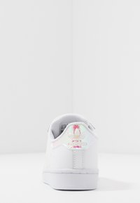 Vit sneaker med iriserande detaljer på hälen och tungan, slät syntetyta, gummisula och texturerad detaljering på mellansulan.