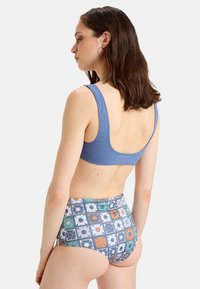 Top de natación azul con espalda tipo scoop, combinado con unas bragas de tiro alto con estampado floral en azul, naranja y verde. Tejido suave y elástico.
