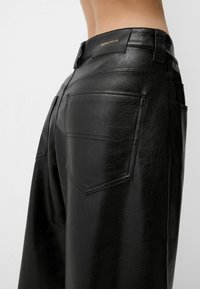 Svarta fuskläderbyxor med hög midja, med bakfickor och en subtil glans. Varumärket "Bershka" präglat på midjebandet.