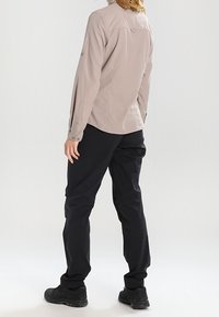 Camicetta grigio chiaro a maniche lunghe con polsini abbottonati, abbinata a pantaloni neri. Entrambi i capi presentano una vestibilità comoda e un tessuto resistente.