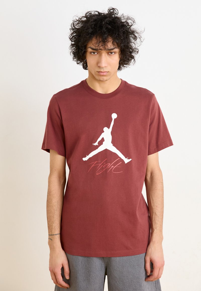 Mørkerød bomulds t-shirt med et hvidt Jordan-logo og ordet "Flight" i en kursiv pink skrifttype. Korte ærmer og rund hals.