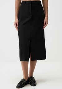 Jupe crayon noire en tissu lisse et structuré, dotée d'une fente avant et de passants de ceinture. Assortie à des mocassins noirs avec des glands.