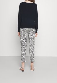 Zwarte gebreide trui gecombineerd met witte streepjesschoenen. De broek heeft een gedetailleerd zwart-wit paisleypatroon. Schoeisel: witte banden.