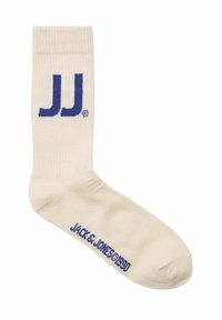 Beige crew sock med blå "JJ" logo ved anklen, ribbet tekstur og "JACK & JONES©1990" tekst langs fodsengen.