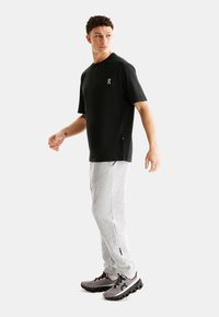 T-shirt de sport noir à manches courtes pour homme avec fentes sur les côtés, pantalon de survêtement gris et chaussures de sport gris-noir avec des détails de semelle prononcés.