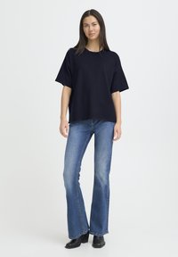 T-shirt oversize bleu marine en tissu doux, associée à un jean évasé bleu clair avec un léger effet délavé et un ourlet net. Bottines à talons noires.