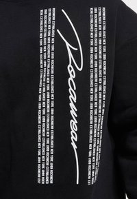 Black sweatshirt featuring bold white text, including "Rocawear" in a stylized script and repeated phrases indicating "Established New York 1999."