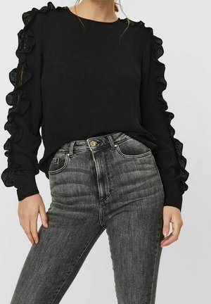 Sort langærmet top med flæsedetaljer langs ærmerne, kombineret med højtaljede mørkegrå jeans. Glat stoftekstur.