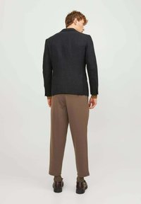 Blazer grigio scuro con texture, a taglio dritto, abbinato a pantaloni marrone a sigaretta. Cuciture visibili e due tasche posteriori sul blazer.