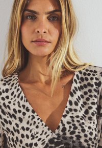 Black and white spotted dress with a deep V-neckline and soft texture. Notable heart tattoo visible on collarbone.