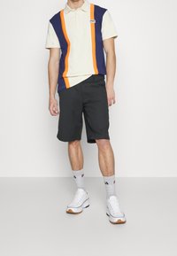 Polo shirt aux couleurs marine et crème avec des rayures orange, associé à un short noir et des baskets blanches. Chaussettes grises avec des accents de logo.
