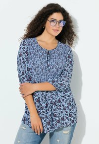 Bluzka w kwiatowy wzór w jasnoniebieskim kolorze z ciemnymi akcentami. Posiada okrągły dekolt, rękawy do łokcia oraz sznurek przy biuście.