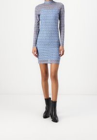 Robe bodycon à manches longues en tissu léger bleu clair avec des logos "HUGO" répétés. Accompagnée de bottines à talons noires.