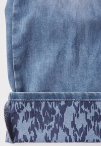 Lichte blauwe denimstof met een donkerblauwe luipaardprint aan de onderkant. De omslag heeft een licht rafelig randje.