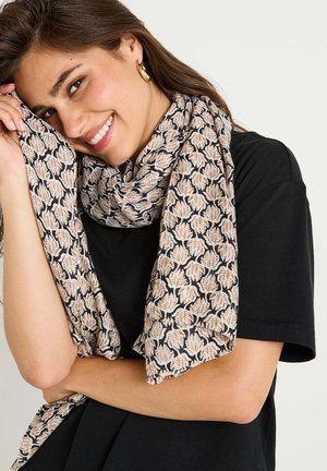 Écharpe légère avec un motif floral en beige et noir, drapée autour du cou. Assortie à un t-shirt noir pour le contraste.