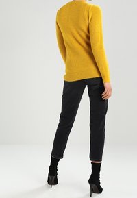 Yellow ribbed knit sweater, long sleeves, round neckline, paired with dark slim-fit jeans and black high-heeled ankle boots.