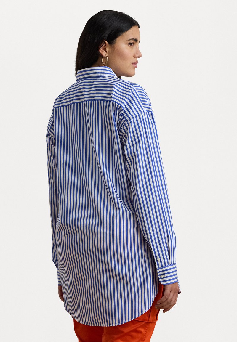 Camisa de rayas en algodón azul y blanco con cuello, puños abotonados y un corte relajado, con un dobladillo redondeado y aberturas laterales.