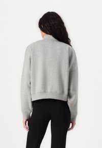 Sweatshirt grigio corto con colletto alto, polsini e orlo a coste. Il materiale appare morbido e strutturato. Indossato con leggings neri.