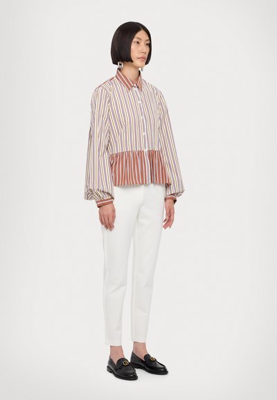 Striped blouse with a peplum hem, featuring long sleeves and a buttoned collar. Paired with slim white trousers and black loafers.