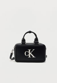 Μαύρη ορθογώνια τσάντα χειρός από γυαλιστερό δέρμα, με διπλές λαβές, αφαιρούμενο ιμάντα και έντονο ασημί λογότυπο "cK" στο μπροστινό μέρος.