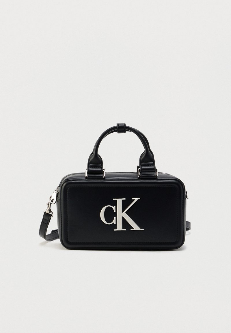 Μαύρη ορθογώνια τσάντα χειρός από γυαλιστερό δέρμα, με διπλές λαβές, αφαιρούμενο ιμάντα και έντονο ασημί λογότυπο "cK" στο μπροστινό μέρος.