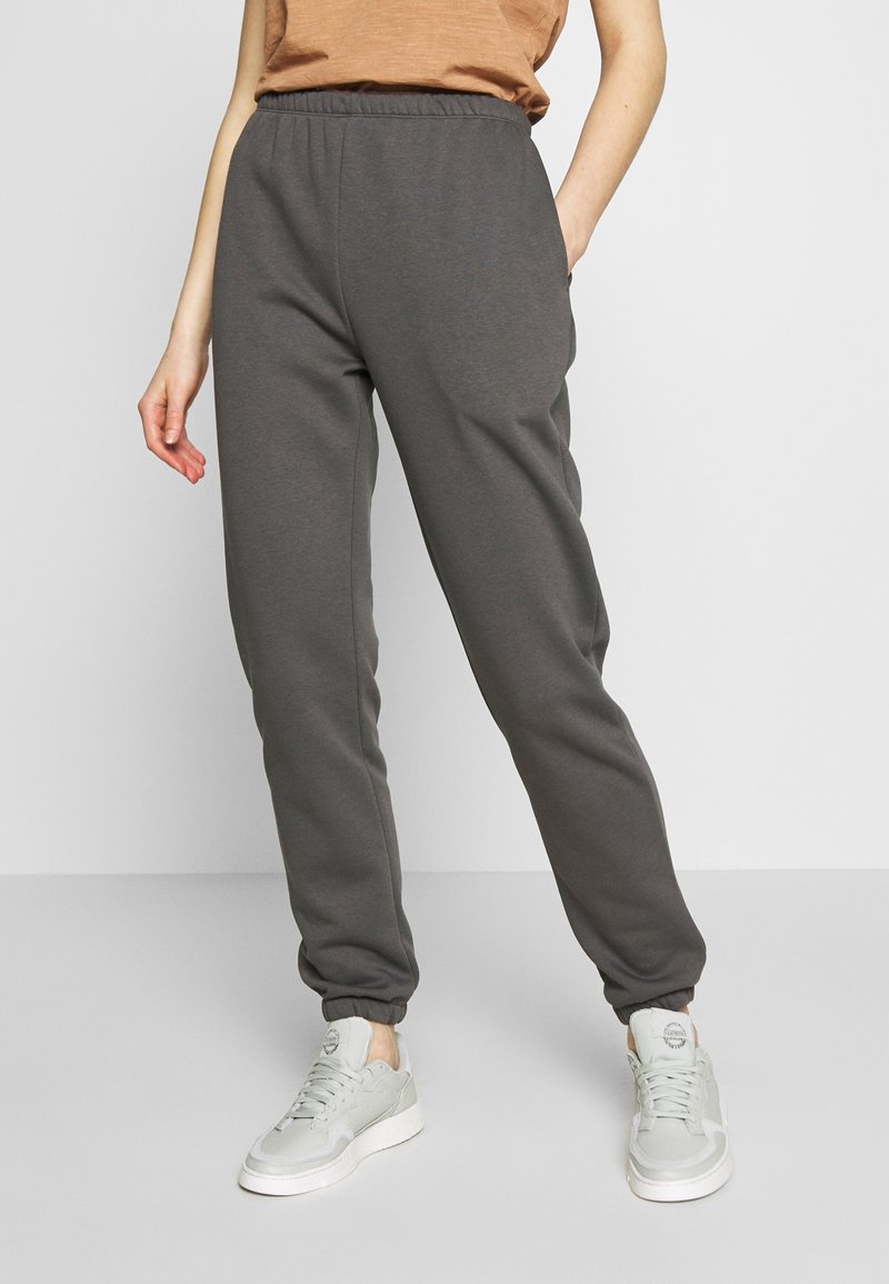 Grå sweatpants med resår i midjan och vid anklarna, tillverkade av mjukt tyg. Bärs med ljusgrå sneakers.