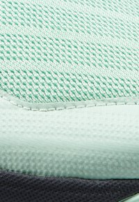 Puntone verde chiaro della tomaia di una scarpa sportiva con design in rete testurizzata. Presenta accenti sintetici lisci, una suola grigio scuro a contrasto e cuciture a vista.