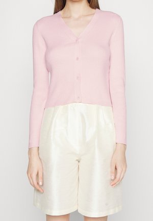 Cardigan rosa a costine con scollatura a V e chiusura a bottoni, abbinato a pantaloni corti in satin crema con vestibilità ampia e vita elastica.