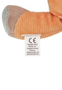 Orange plush toy with corduroy texture, featuring a grey and brown underside. Includes a care label with manufacturer details.