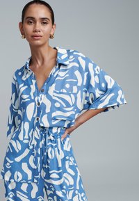 Blue and white patterned linen shirt with short sleeves, a collar, and a chest pocket; paired with matching drawstring waist pants.