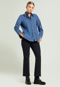 Niebieska koszula z denimu zapinana na guziki, wąski krój z długimi rękawami. Zestawiona z czarnymi dżinsami o prostych nogawkach i czarnymi botkami za kostkę. Gładka tekstura, minimalne detale.