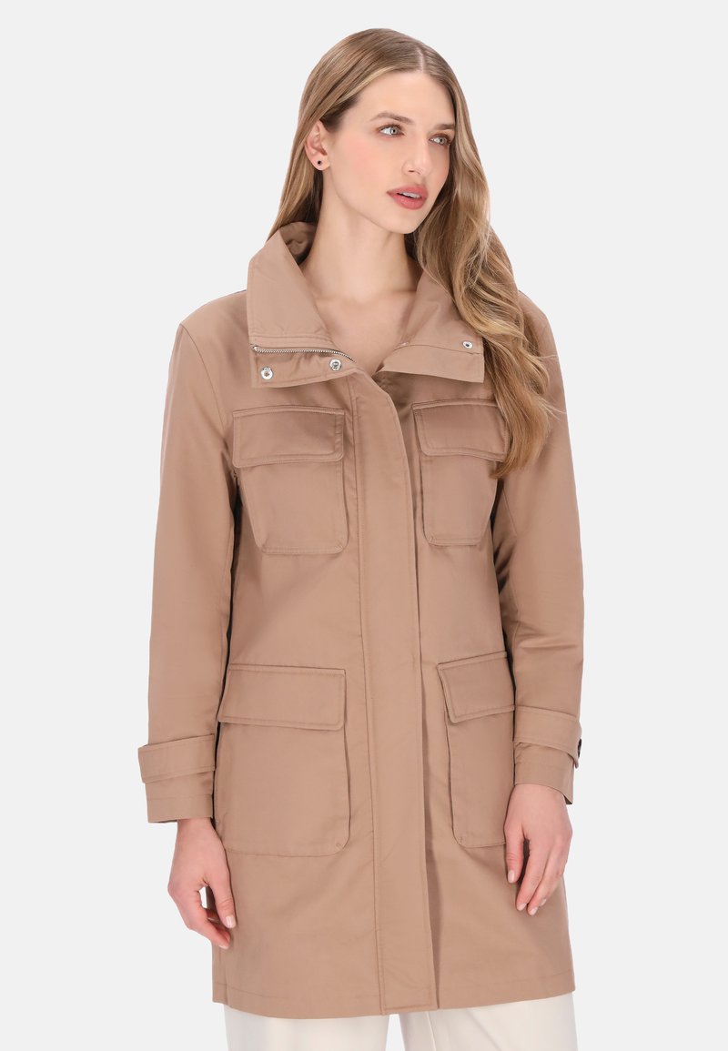 Knælang beige frakke med høj krave, dobbelte brystlommer og trykknaps-/knapdetaljer. Fremstillet af glat stof med en afslappet pasform.