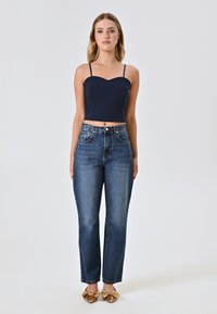 Crop top blu navy con spalline sottili, jeans blu a vita alta e scarpe flat con dettaglio a fiocco dorato. Design semplice, texture denim classica.