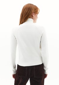 Witte gebreide coltrui met geribbelde zoom en manchetten, met raglanmouwen en een zachte textuur, gedragen met donkerbruine corduroy broek.