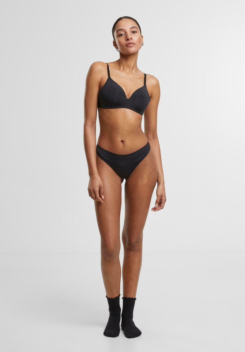 Fekete sima szövetből készült melltartó és bikini szett, V-nyakú melltartóval és alacsony derekú bugyival. Egyszerű dizájn vékony pántokkal és varrás nélküli szélekkel.