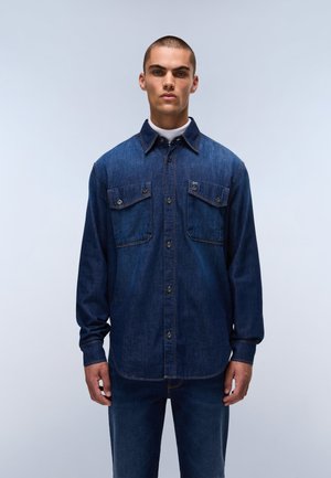Denim shirt in dark blue with long sleeves, button front, two chest pockets, and contrasting stitch details. Smooth texture and relaxed fit.